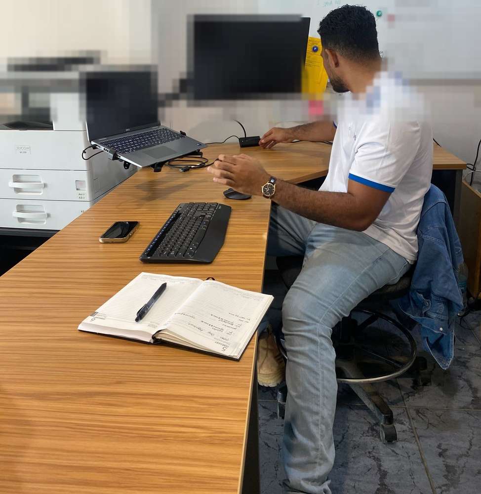 A WanTok team member at a desk with a planner, keyboard, and laptop