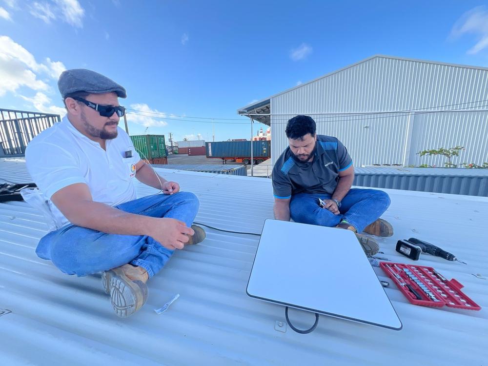 Two WanTok technicians seated on a rooftop setting up a wireless dish beside their toolkit