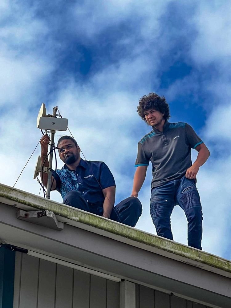 Two WanTok technicians on a rooftop aligning a wireless signal dish